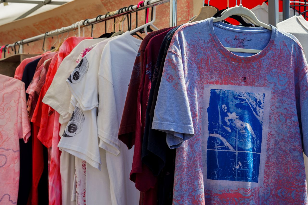 why-choose-us A vibrant display of assorted t-shirts hanging in a market setting, perfect for fashion enthusiasts.