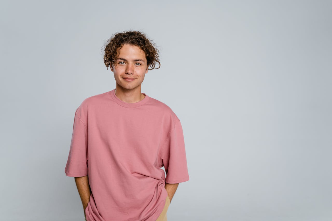 who-we-are Smiling young adult wearing a pink t-shirt in a studio setting. Perfect for lifestyle or fashion themes.